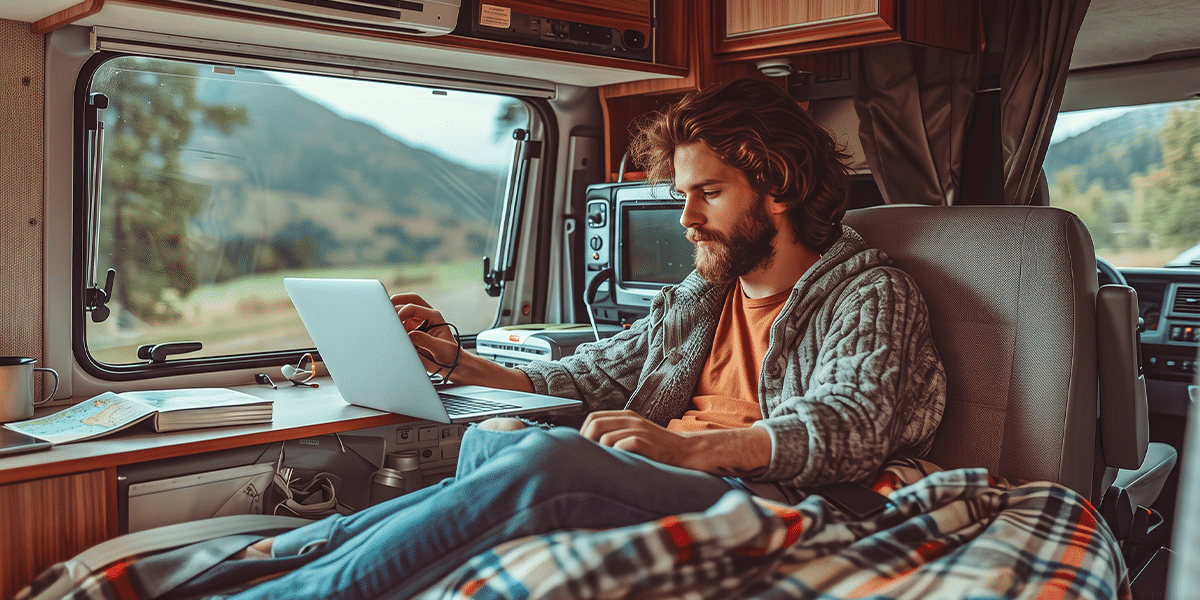 Man working on a laptop inside an RV with mountain views through the window