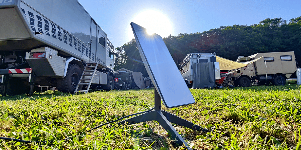 Starlink satellite dish set up on the grass at a campground with overland RVs parked behind it